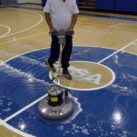 Man scrubbing a gym floor with an automatic scrubber.